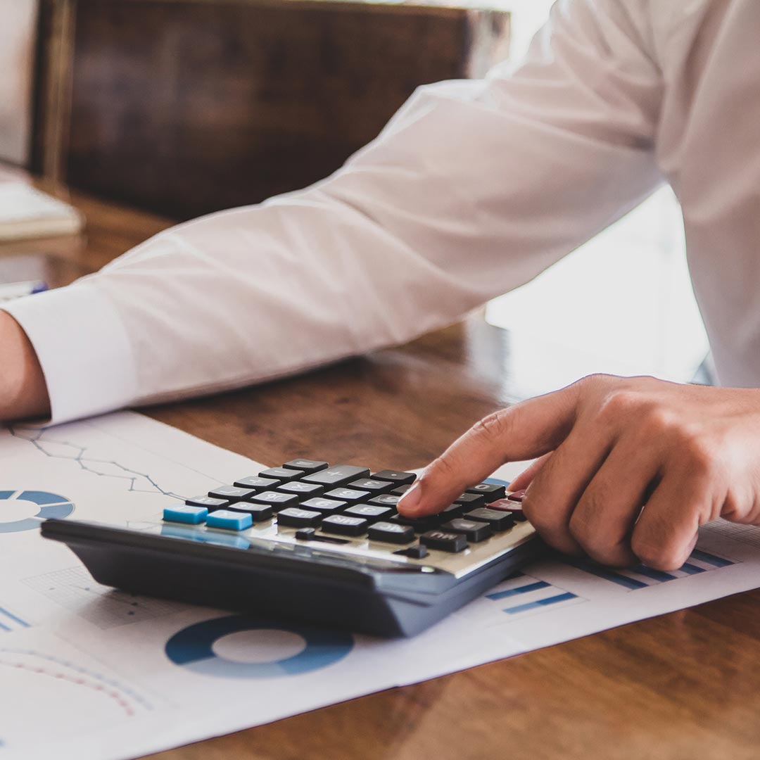 person sitting at desk using calculator with papers full of pie charts underneath calculator